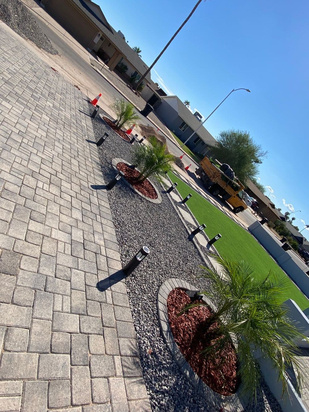 Landscaped front yard with paver stones, palm trees, and decorative rocks under a clear blue sky.