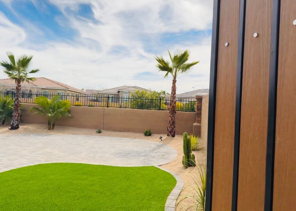 Lush backyard with artificial grass, palm trees, and a serene landscape under a blue sky.