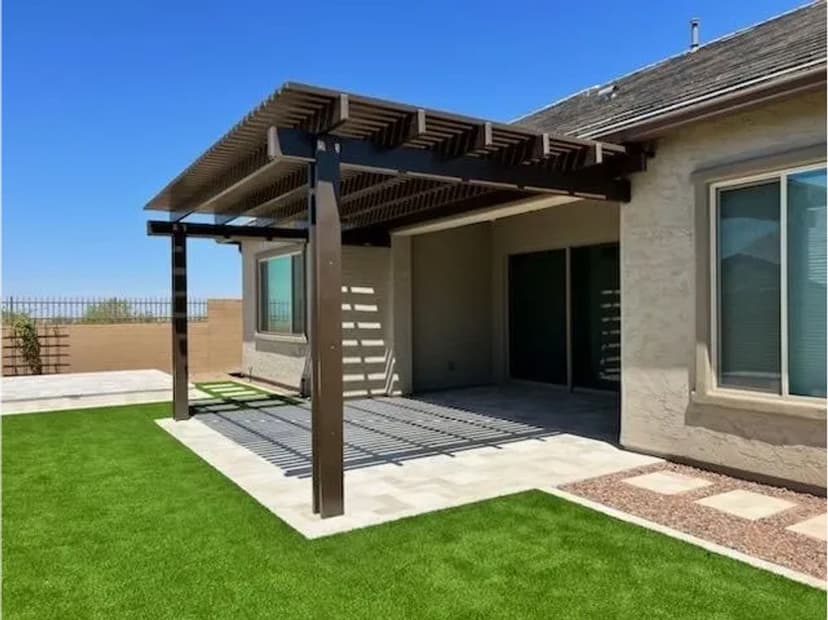 Modern backyard with a shaded patio, artificial grass, and a clear blue sky.