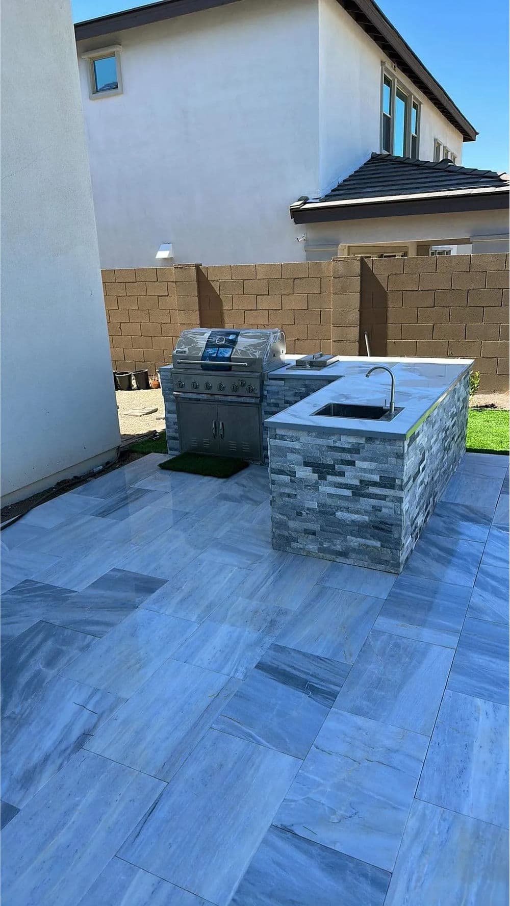 Modern outdoor kitchen featuring a stone grill station and sleek marble flooring.