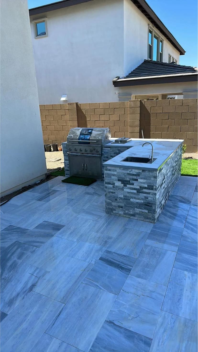 Modern outdoor kitchen with a grill and stone counter on a marble patio.
