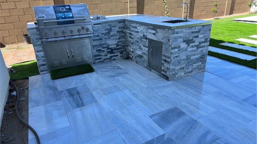 Outdoor kitchen featuring a stone countertop, stainless steel grill, and modern flooring.